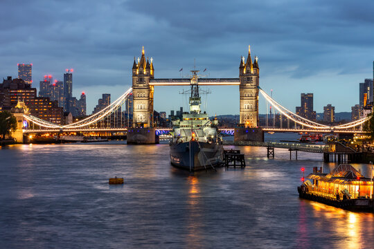 Tower Bridge and Belfast warship on Thames river at night, London, UK - Powered by Adobe