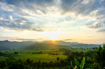 The beautiful landscape of the sunrise, The sun's rays through the clouds at the top of the hill and the Rice fields, in Chiang Rai Thailand