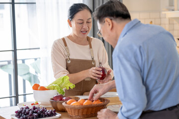 A woman prepares fresh vegetables in a cozy kitchen, while a man assists in the background. The scene emphasizes a warm and healthy lifestyle with a focus on fresh produce and home cooking.