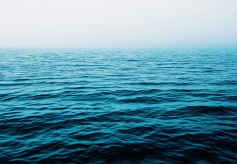 Obraz premium A serene view of the ocean, featuring calm blue waves under a misty sky. The image captures the tranquil essence of nature, perfect for relaxation and reflection.
