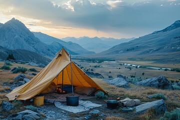 A warm yellow tent is pitched in a vast valley surrounded by mountains during sunset. Cooking gear and a cozy setup invite relaxation amid the natural beauty