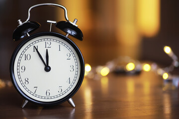 Vintage Black Alarm Clock on Wooden Table with Blurred Warm Lights in Background