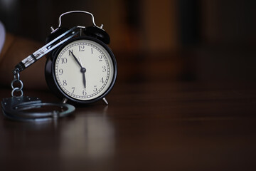 Vintage Alarm Clock and Handcuffs on Wooden Table Representing Time and Imprisonment