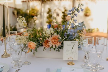 Floral centerpiece featuring peach, yellow, blue, and white flowers in a rectangular vase.