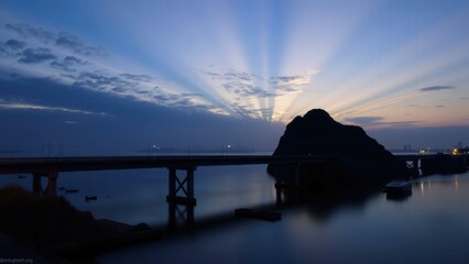 Serene Sunset Over Calm Waters: Bridge Silhouette and Rock Formation at Twilight