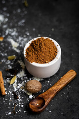 Selbstgemachte Spekulatius Gewürzmischung in kleiner Schale mit Holzlöffel, Puderzucker, Zimtstange, Kardamon Nelke und Muskatnuss