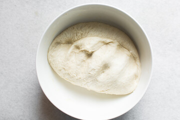 Overhead view of challah dough in a white mixing bowl, top view of homemade challah dough resting in a white mixing bowl, process of making challah
