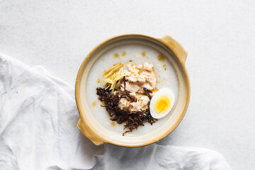 Overhead view of rice chicken congee with ginger and caramelized onions in a clay pot, top view of rice and chicken porridge, chinese chicken congee, korean dak juk or japanese okayu in a claypot
