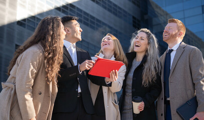 Group of business people teammates are happy celebrating their success on year results laughing outdoors in a tablet