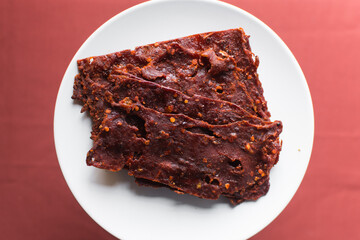 Overhead view of Nigerian kilishi on a white plate, top view of nigerian spicy beef jerky, flatlay of dried beef suya