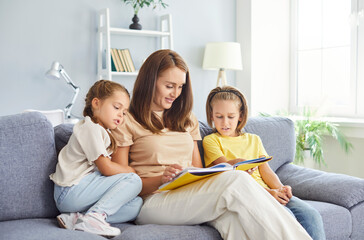 Happy family couch sitting reading book, kids, happy mom enjoying leisure at home together, interesting fairy tale, child education and development with parent, attentive listening telling story 