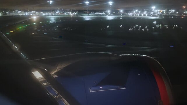 The plane lands at the airport at night. Pov of a passenger through a porthole window onto the wing of an airplane with a red blue engine that lands on the runway at night. Film grain texture