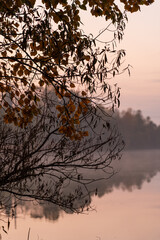 Early morning tranquility at a serene lake with autumn foliage and a distant smokestack reflecting in the calm water