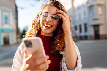 Woman using smartphone while standing outdoors at sunset. Technology, connection, blogging, modern lifestyle concept