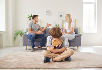 Sad little child crying as parents fight and argue in the background at home. The conflict causes...