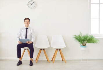 Man job seeker sitting in office with empty chairs waiting for interview invitation turn and looking at camera. Company employee preparing for meeting or conference. Recruitment and business concept.