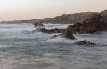 Time-lapse photo of ocean waves crashing on the shore, showing the fluid motion and energy of the water as it ebbs and flows, creating a mesmerizing effect of perpetual motion and natural rhythm
