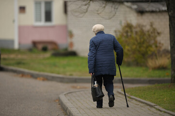 a lonely elderly woman with a cane walks down the street and carries a bag