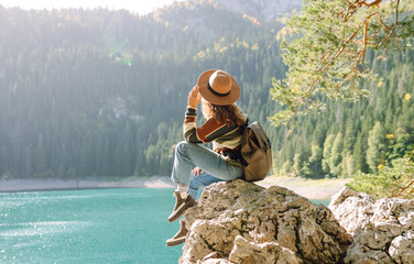 Female traveler enjoying the view of Lake among mountains. Hiking with backpack. Active lifestyle.