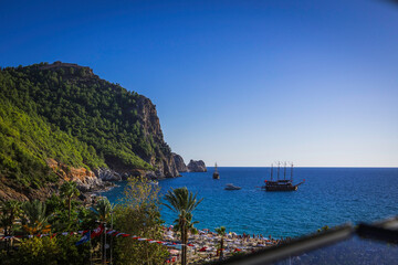 Naklejka premium Alanya castle top view on the mountain with coast ferry boat on blue sea . Beautiful cleopatra beach Alanya Turkey landscape travel landmark.