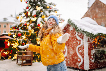 Young woman laughs and throws snow in a winter on Christmas market. Lights around. Winter holidays.