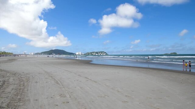 View of Enseada Beach, a beautiful beach with view to the sand, the sea on a blue sky day and few clouds. Guaruja - SP, Brazil.