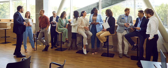 Diverse multinational business people men and women chatting after a meeting. Company employees or group of staff talking with each other in the office during the break in meeting room. Banner.