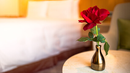 A bedroom with white bed and a table holding a gold vase with a single rose.