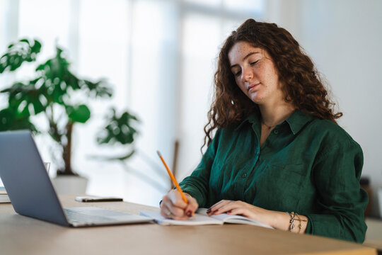 Thoughtful young woman holding studying, with a laptop and notebook in front of her