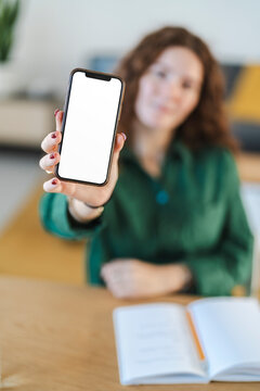 Young woman holding up a smartphone with a blank screen in a relaxed home office environment