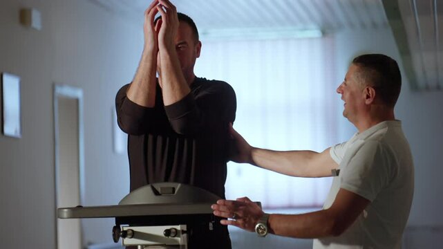 Patient, guided by a physiotherapist, performs arm mobility exercises using a specialized support bar. Concept of physical rehabilitation, patient care, recovery, shoulder injury