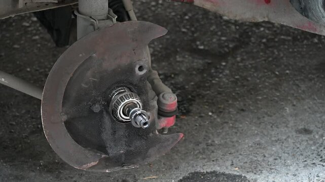 Car with Wheel Removed Exposing Brake and Suspension. Close-up of a car missing a wheel, showing the exposed brake rotor, suspension, and wheel well in a repair or maintenance setting.

