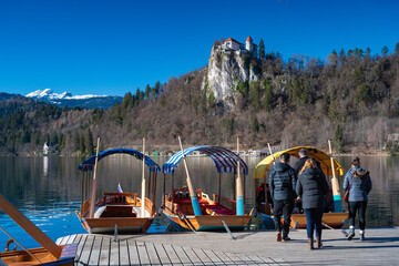 Touristen und Ausflugsboote auf dem See in Bled, im Hintergrund Burg Bled und die Alpen, Slowenien