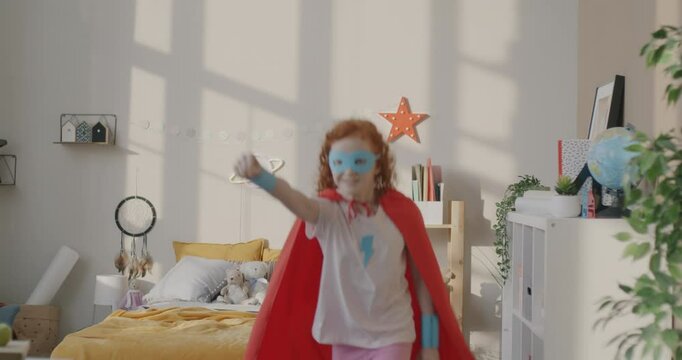 Slow motion of hyperactive girl in superhero costume jumping on bed running in bedroom playing funny game at home. Childhood and fun concept.