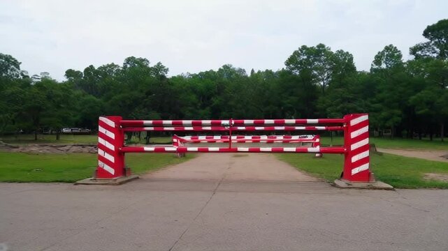 A red-striped barrier gate marks park entrance, surrounded by lush greenery, conveying a calm and secure atmosphere.