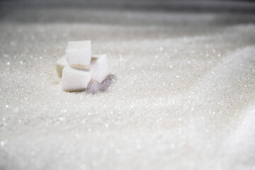 Sugar cubes on a pile of white refined granulated sugar, close up. Weight gain and risk of heart...
