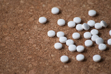 A pile of round white pills on a wooden background. The pills are scattered on the surface.