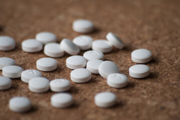A pile of round white pills on a wooden background. The pills are scattered on the surface.