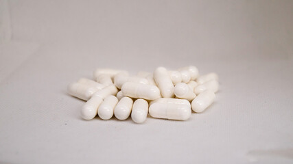 White pills scattered on light background. Close-up of pharmaceutical capsules on plain surface. Pile of white medication tablets isolated
