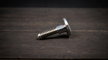 Screws and bolts for furniture repair. A shiny metallic bolt rests on a dark wooden surface, showcasing its detailed threading and smooth, polished head.