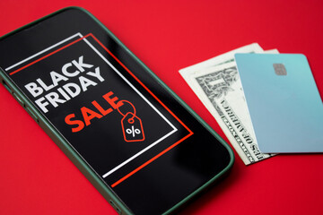 Close up of a smartphone screen displaying a Black Friday online sale on red background with credit cards and money