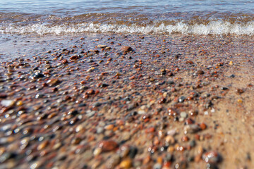 Obraz premium A pebble sea shore with a foaming wave of water. Low angle photo in close-up, low depth of field, nice blur and bokeh