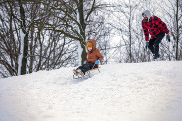 A little boy sliding down a hill with a sled. Winter outdoor fun with cool daddy