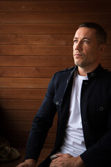 Handsome businessman in casual dark blue blazer and white t-shirt planning business idea and looking up to the side as lifestyle entrepreneur portrait with wooden wall on background