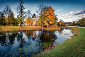 Wonderful morning view of Palace Olszanica on the shore of small river. Stunning autumn cityscape of Olszanica town, Poland, Europe. Trees covered with orange and crimson leaves..