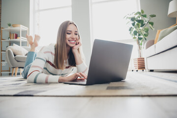 Fototapeta premium Young woman enjoying leisure time at home with a laptop in a cozy and natural daylight living room setting