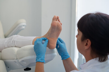 A podologist wearing gloves glues a special relief corn patch on the heel of the patient. Patient on medical pedicure procedure, visiting podiatrist. Peeling feet. Foot treatment in SPA salon.Podiatry