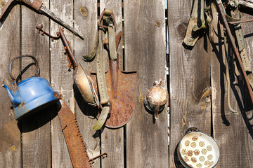 Flea market background. Historical everyday tools. Wheel, lantern, horseshoes. Traditional agricultural implements. Life in past centuries texture. Wooden wall antique items.