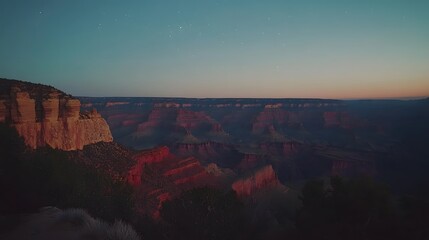 Fototapeta premium Majestic canyon at sunset with red rock formations glowing warmly in the fading light, and a clear, starry sky overhead. The scene captures the grandeur and tranquility of nature at dusk.