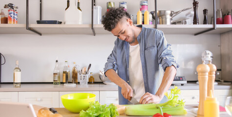 Young African-American man cooking in kitchen